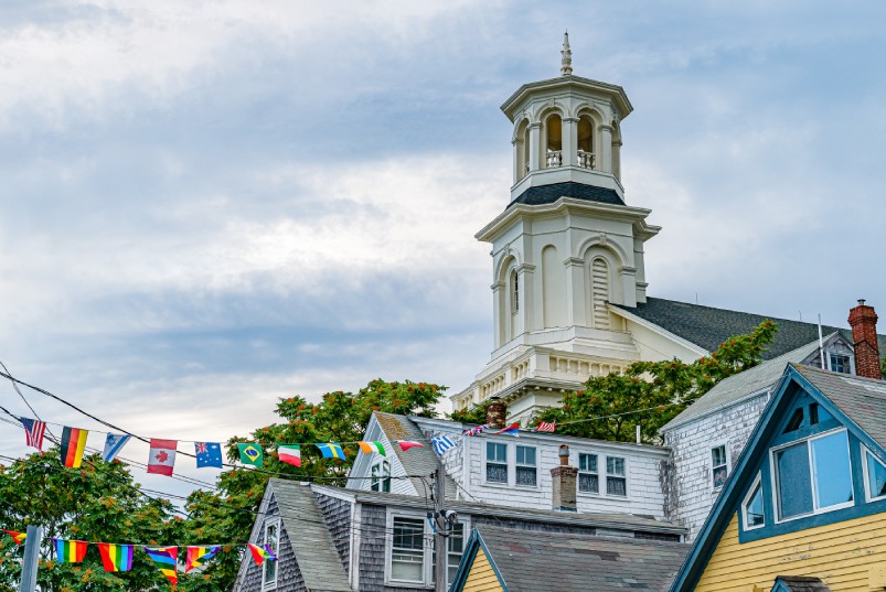 The Provincetown Public Library towering over a few other downtown buildings with various flags strung in the air.