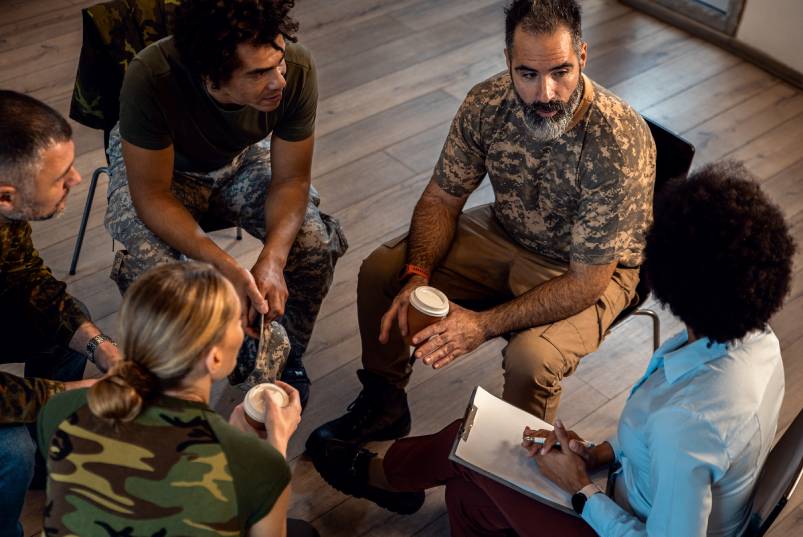 A diverse group of veterans sitting in a group circle and having a discussion while drinking coffee.