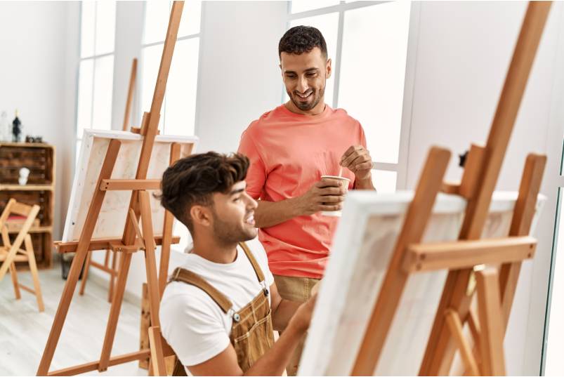 Two young men smiling at each other as they spend time working together in a professional painting studio.