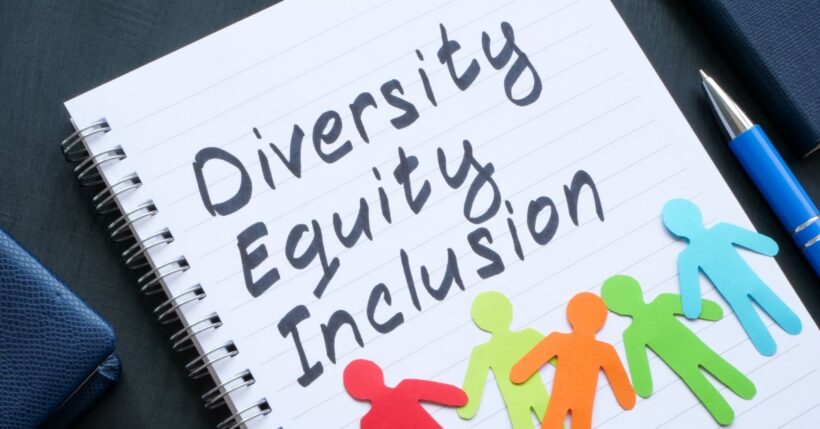 A notebook with "diversity, equity, inclusion" written in bold black letters. There are people paper cutouts on top.