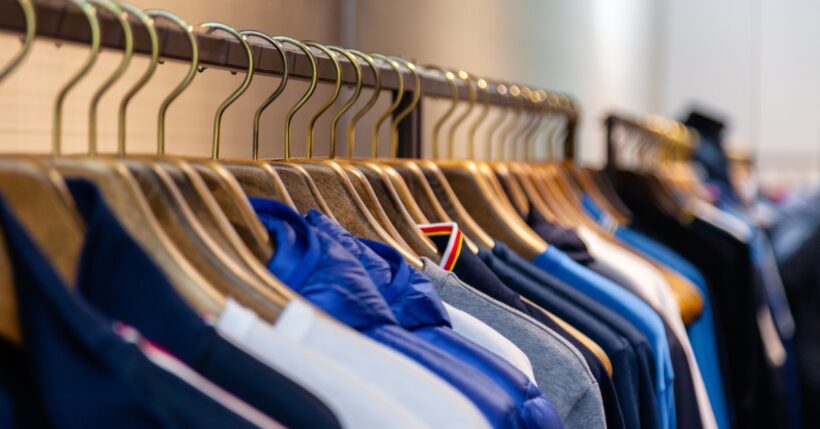 Rack full of hangers, each one holding a top piece of clothing with a mirror in the background reflecting them.