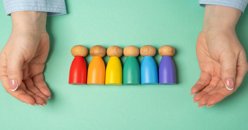A pair of hands cupped on either side of a row of pawn-shaped figures painted to form a rainbow.