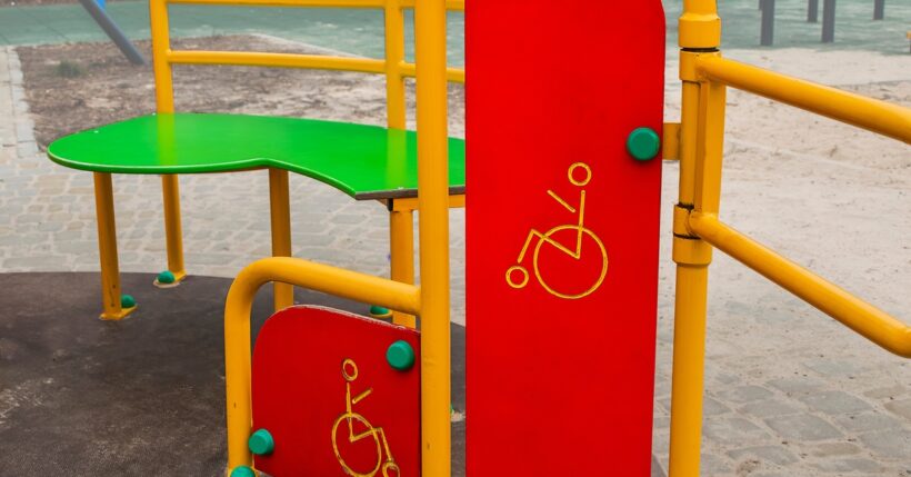 A red, green, and yellow piece of playground equipment with images of wheelchairs engraved on the side.