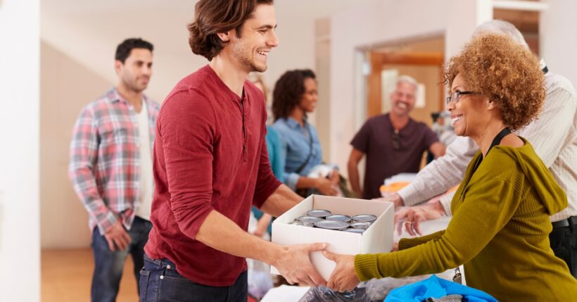 A person donating a box of canned goods to a friendly neighborhood mutual aid or charity effort.