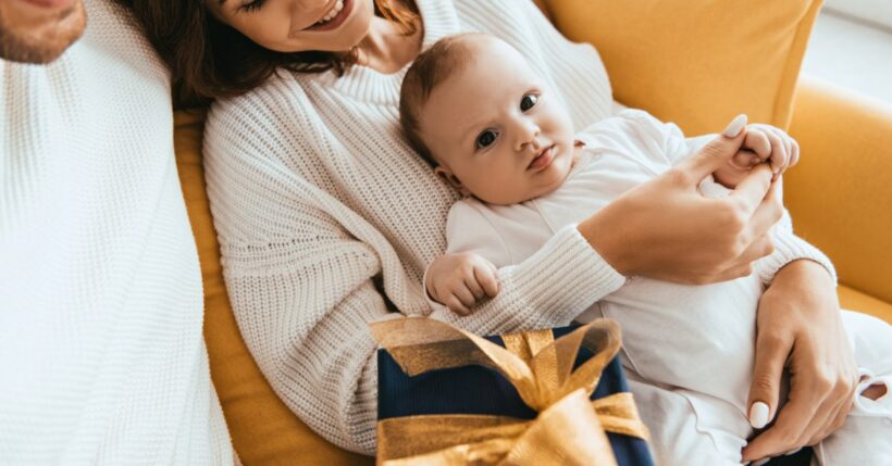 A man and a woman laying next to each other with a baby on the woman's chest. A present is next to the baby as well.