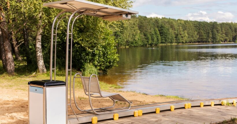 Accessible lakeside dock with adaptive transfer chair under canopy beside calm water and tree-lined shoreline.