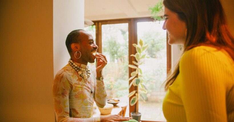 A pair of friends smiling and laughing while hanging out together in a space with warm, natural lighting.