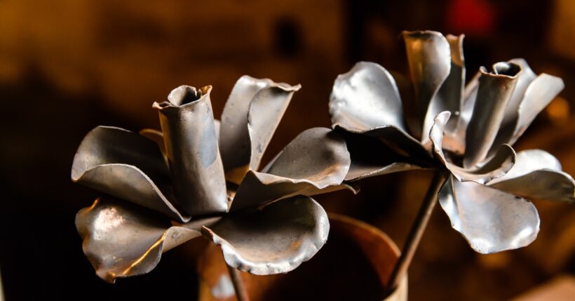 A pair of large flowers made out of shaped metal pieces. The flowers are placed inside of a ceramic flower vase.